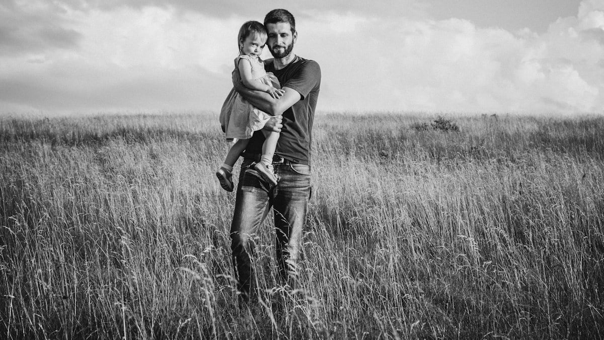grayscale photo of couple hugging on grass field